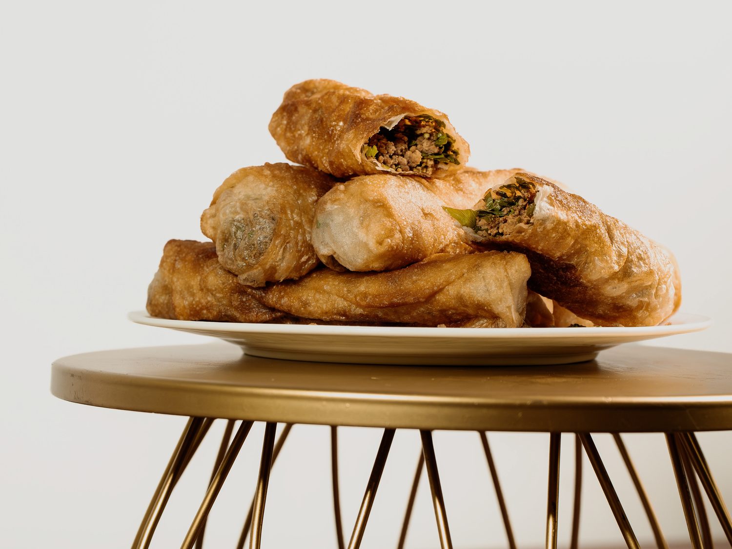 Iraqi Bourak, crisp pastry rolls stacked on a gold serving stand with one opened to show the filling