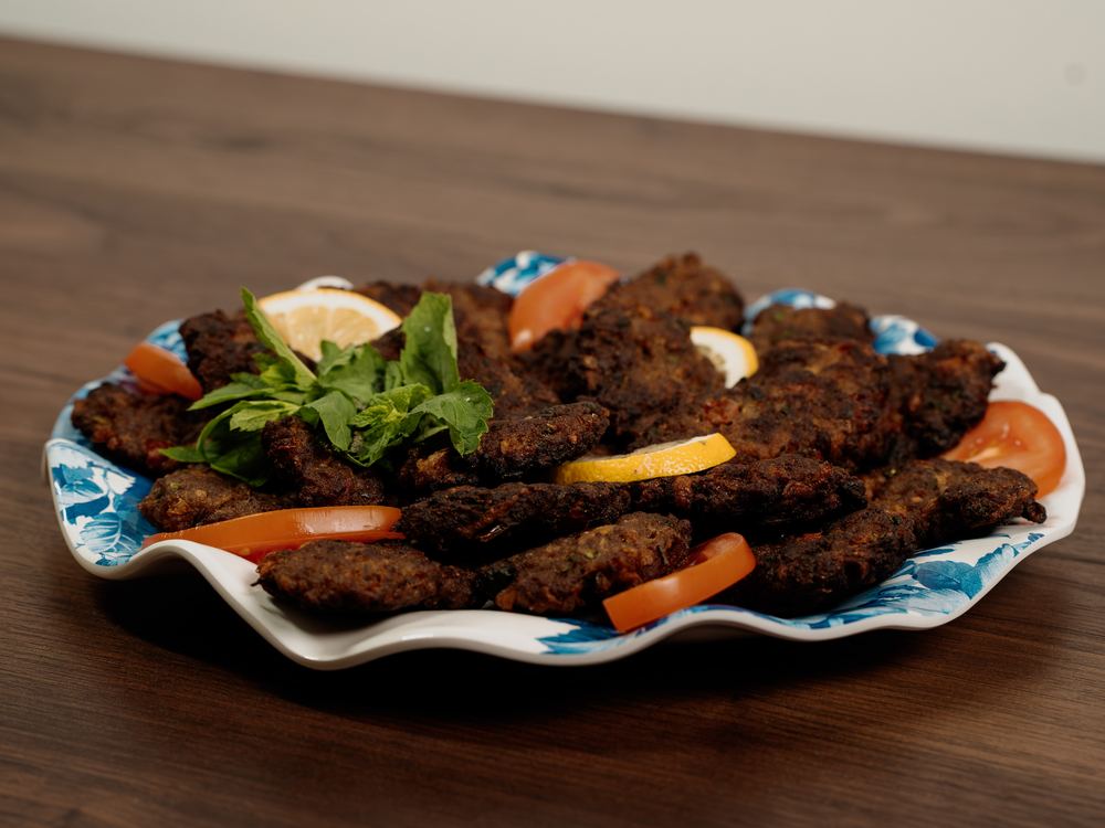 Kabab Arooq on a blue and white platter with tomato and herbs