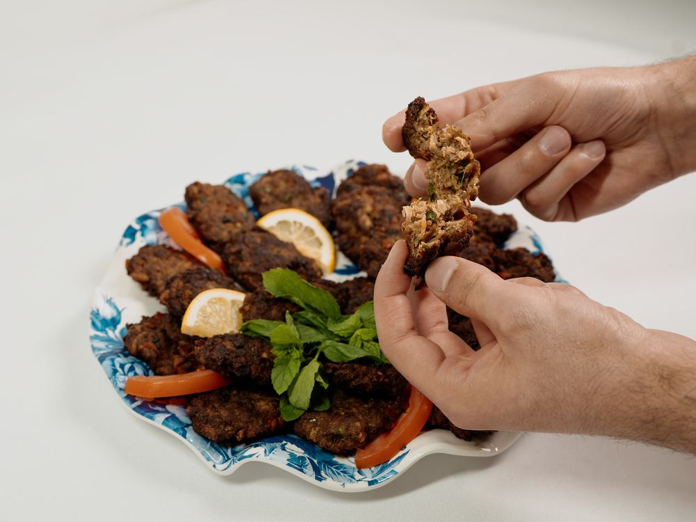 A hand lifting a piece of Kabab Arooq from the platter