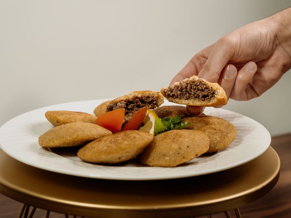 A hand holding an opened Kubba Jareesh above the plate